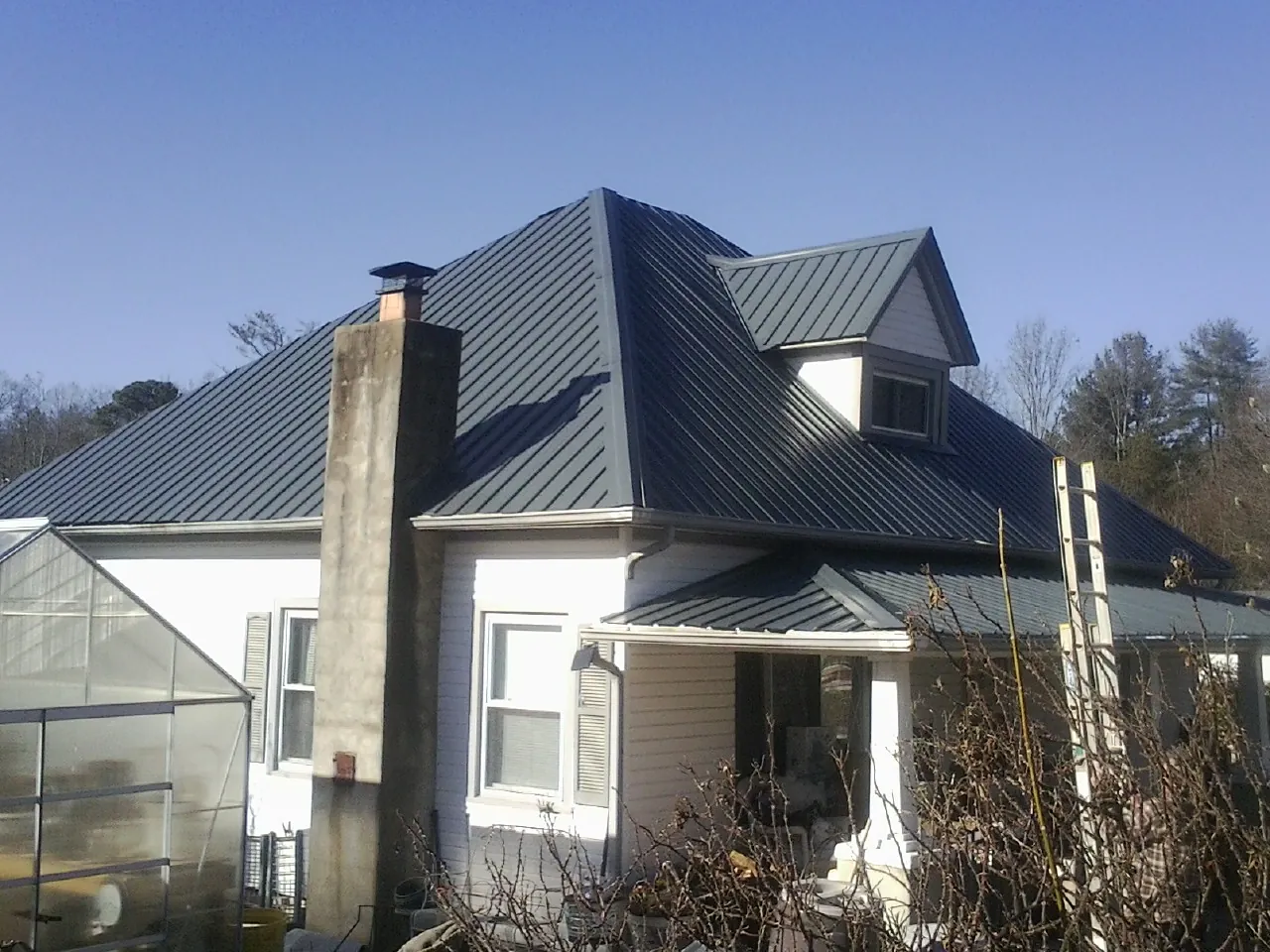 Dark blue standing seam metal roof on a white farmhouse with dormer — Slate & Tile Roof Repair by Roofing Brothers in Torrance