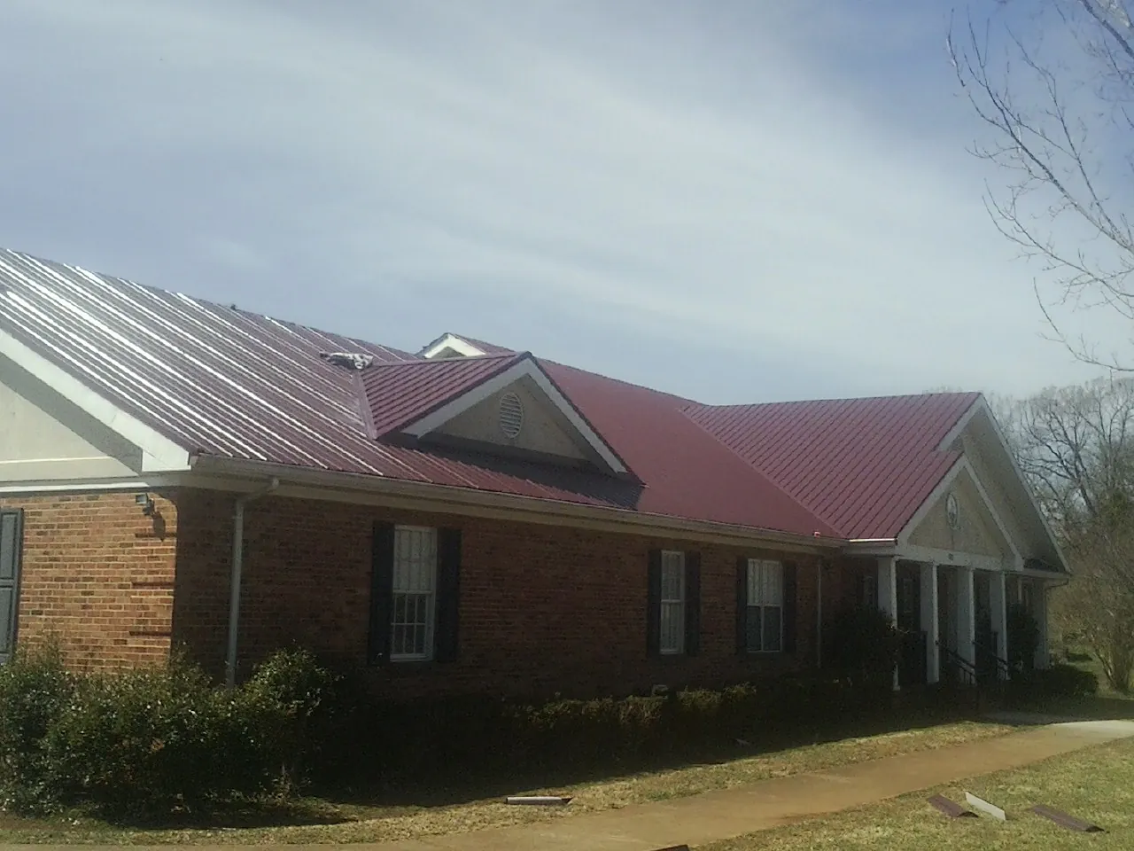 Red metal roof with gabled entries on a long brick building, from a Hail Damage Roof Repair job in Torrance