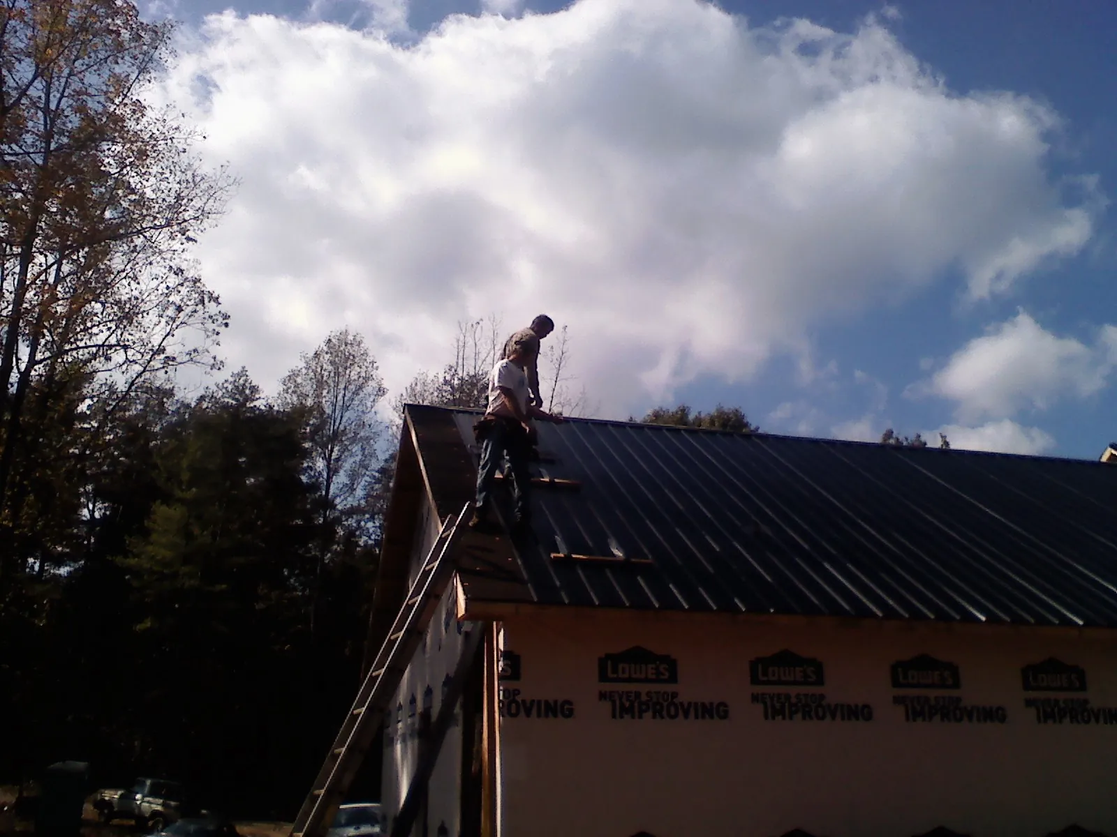 Roofer fastening dark metal panels high against a cloudy sky, from a Roof Inspection job in Torrance